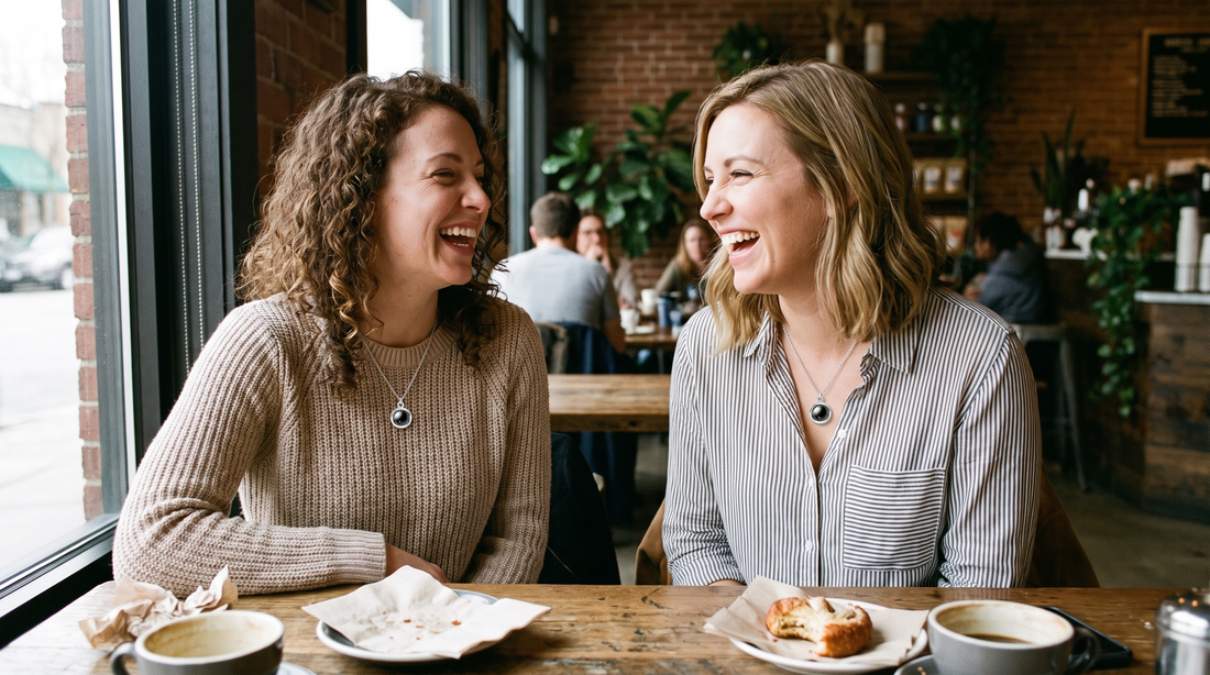 Two women wearing matching circle lens pendant necklaces at a cafe table