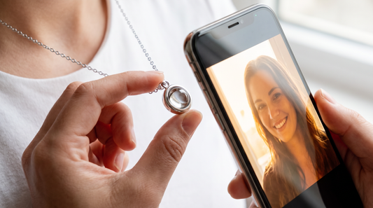 Close-up of a silver circle pendant with a phone camera pressed against the stone revealing a portrait photo on screen, demonstrating how photo projection jewelry works