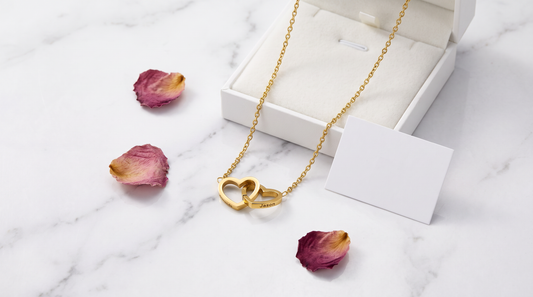 Engraved double heart gold necklace flat-lay with rose petals showing personalized engraving detail