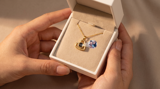 Hands opening a gift box revealing a gold heart pendant necklace