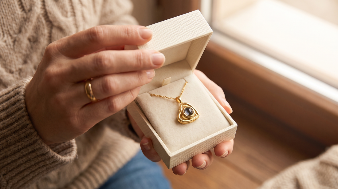 Hands wearing a wedding ring opening a gift box with a gold heart pendant necklace