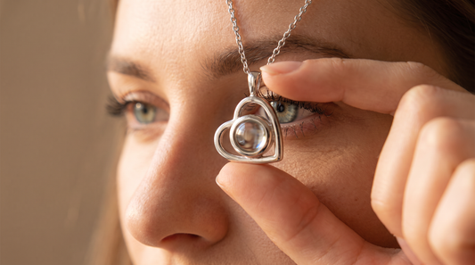 Woman holding a Dazzle Wears silver heart pendant up to eye level and looking directly into the glass stone to see the hidden photo inside