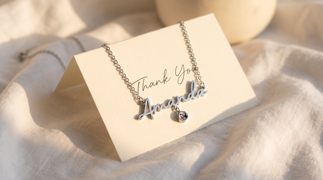 Personalized teacher gift jewelry: name necklace with photo charm on a teacher's desk beside an apple and thank you card