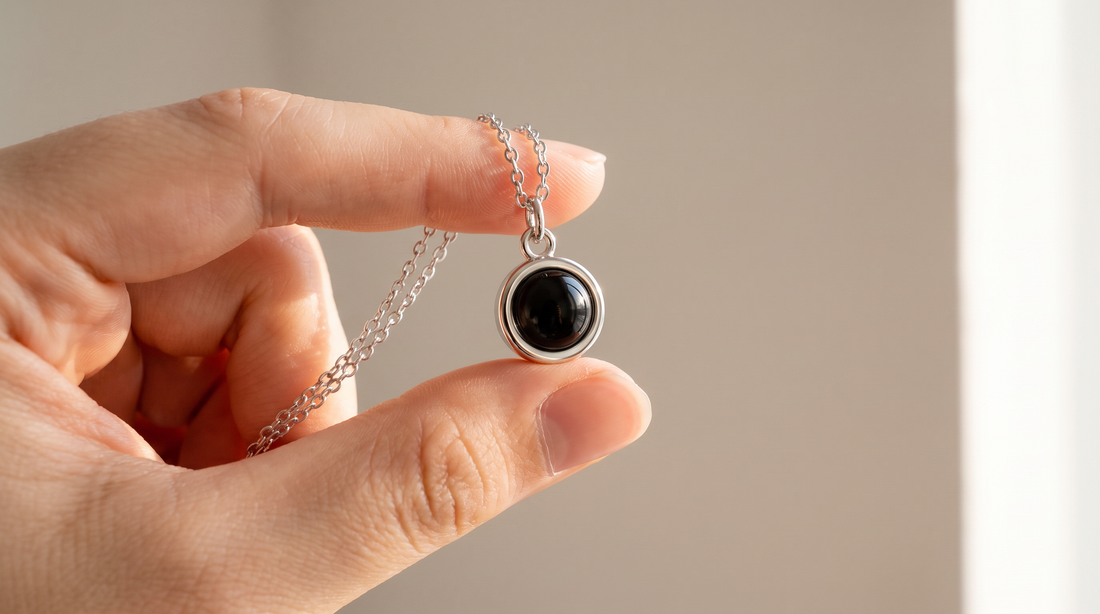 Circle lens pendant necklace held between two fingers in soft light