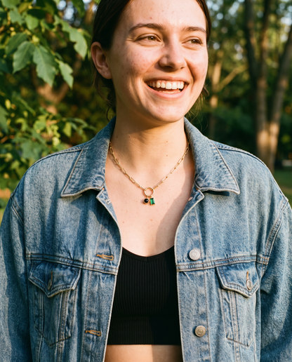 Young woman wearing personalized birthstone charm necklace, paperclip chain, denim jacket outdoors